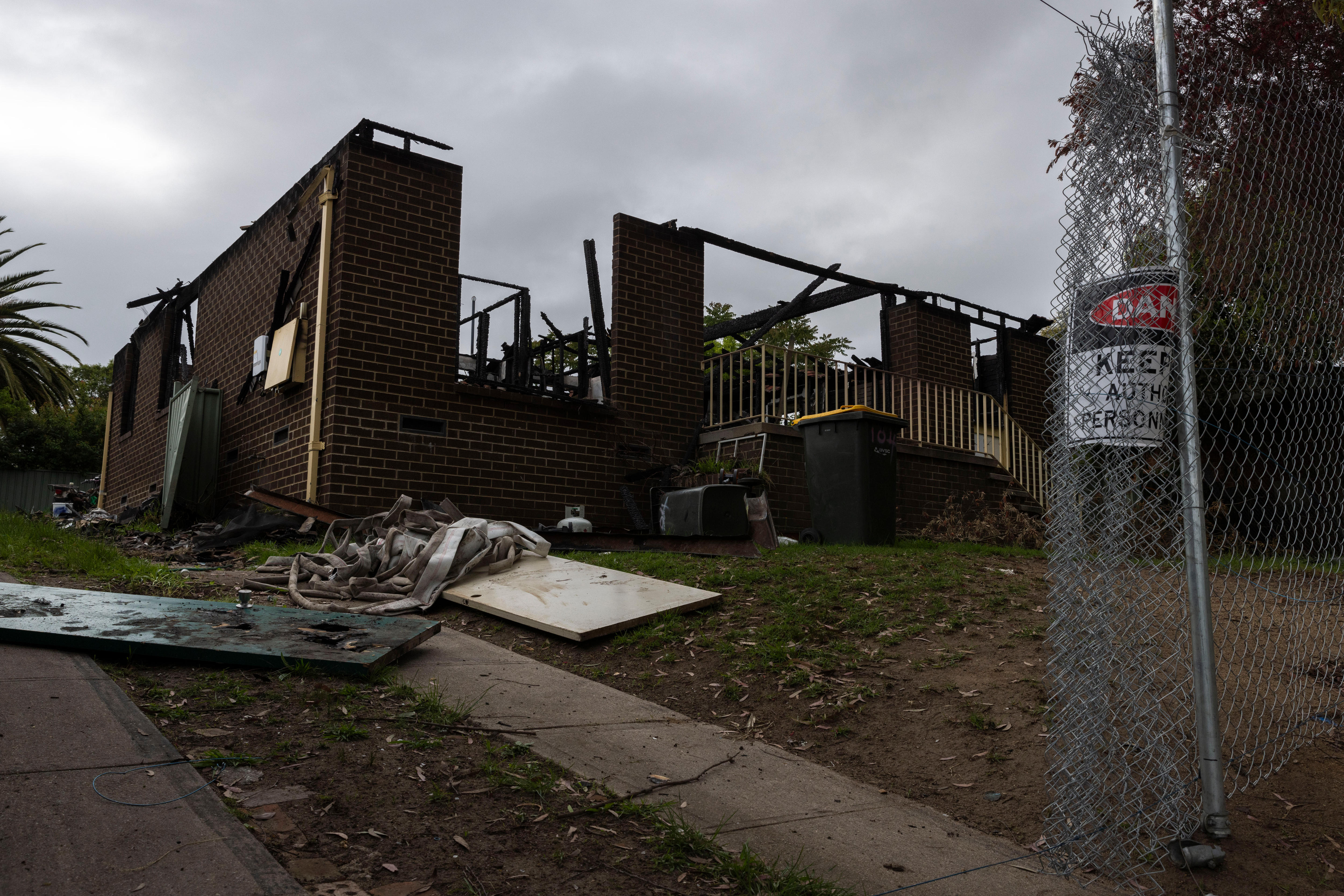Os restos de uma casa queimada atrás de uma cerca de arame. 