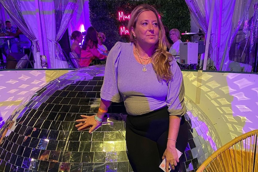 A woman leans against a giant disco ball 