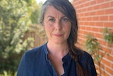 Chloe Adams stands in her garden wearing a denim shirt with an Extinction Rebellion badge.