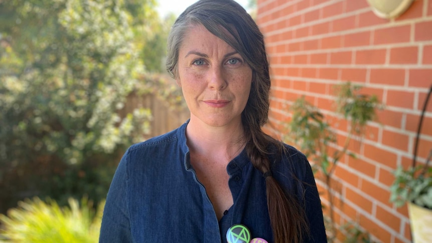 Chloe Adams stands in her garden wearing a denim shirt with an Extinction Rebellion badge.