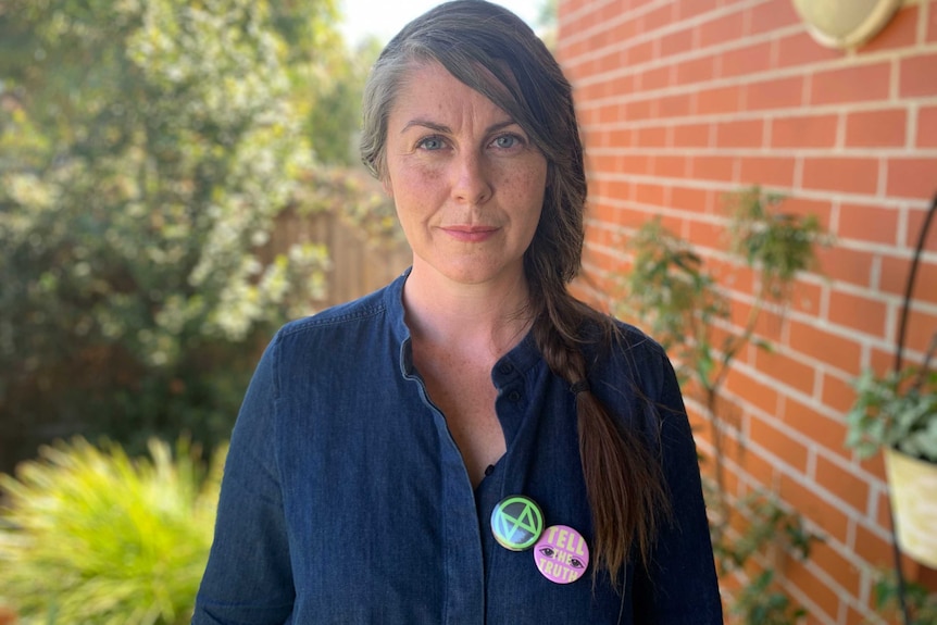 Chloe Adams stands in her garden wearing a denim shirt with an Extinction Rebellion badge.