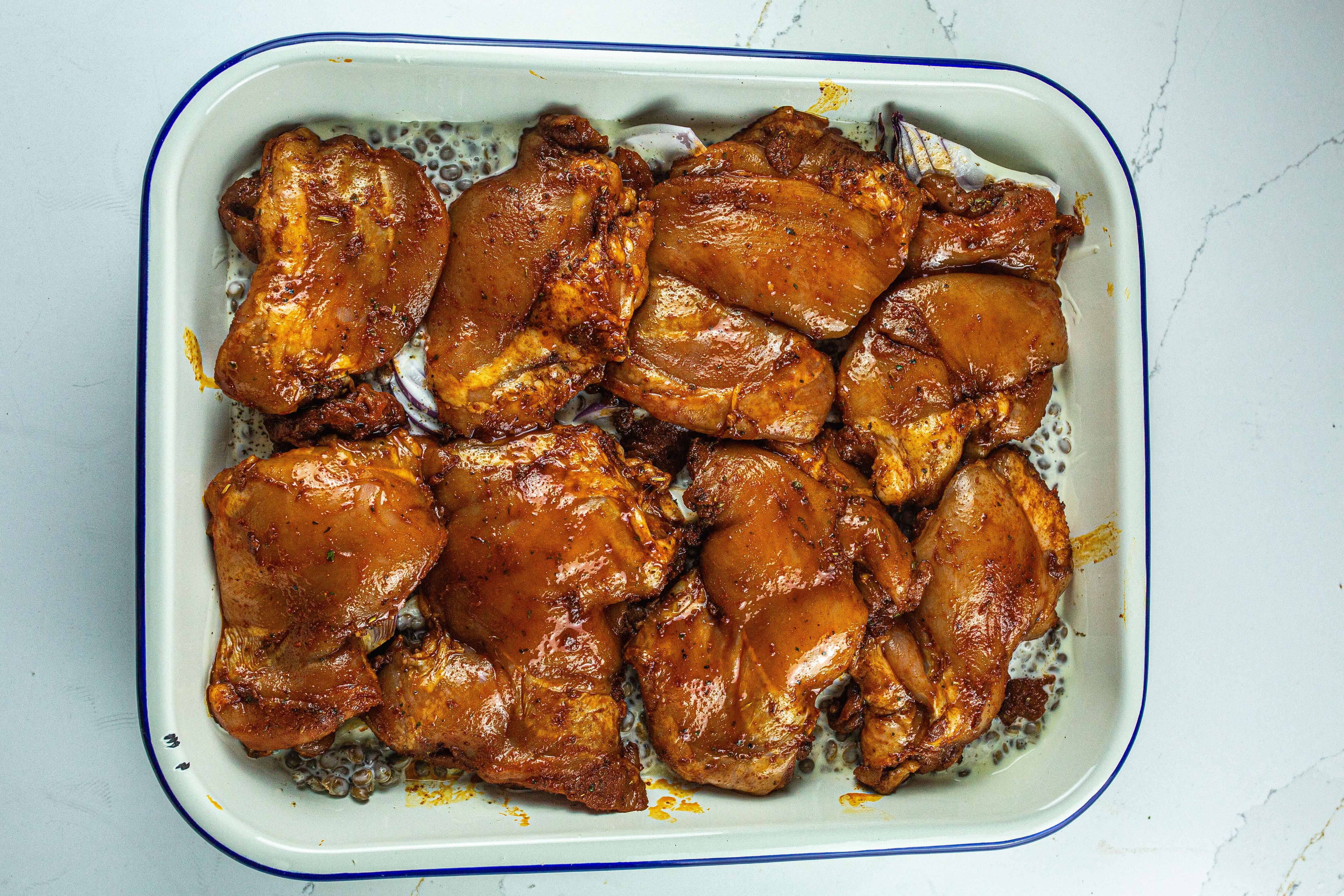 Eight seasoned chicken thighs sit on top of lentils mixed with cream, ready to be baked.
