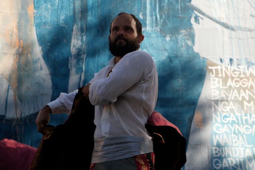 A man in a Spanish toreador costume in front of a blue wall with indigenous names