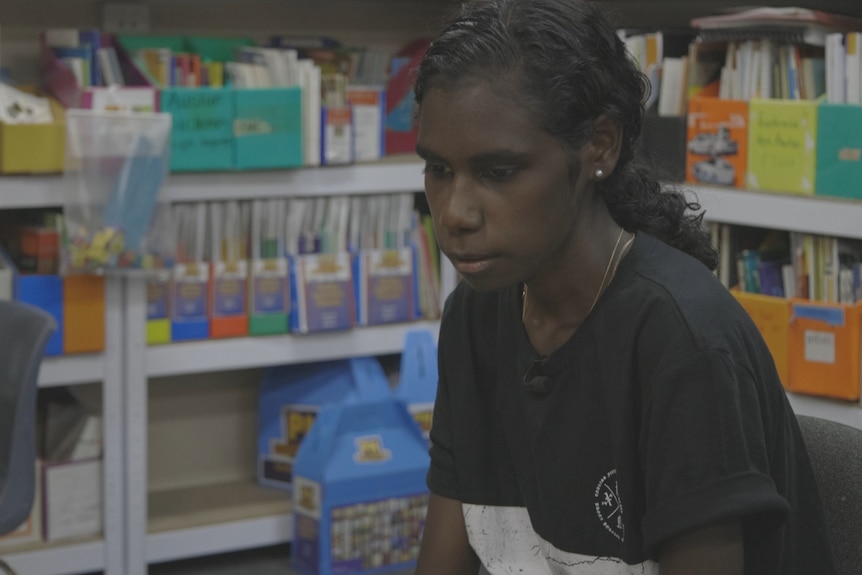 A young girl looks serious. She is in a classroom.