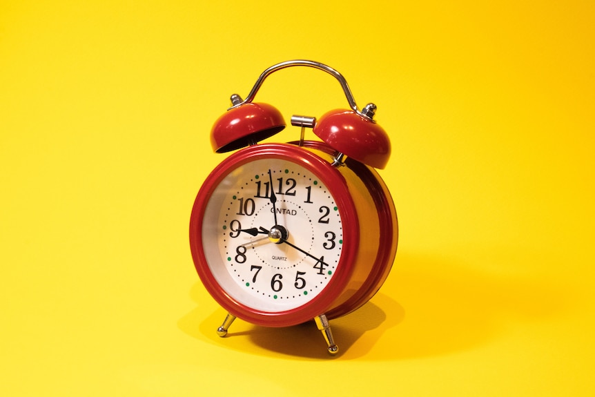A red alarm clock on a yellow background. 