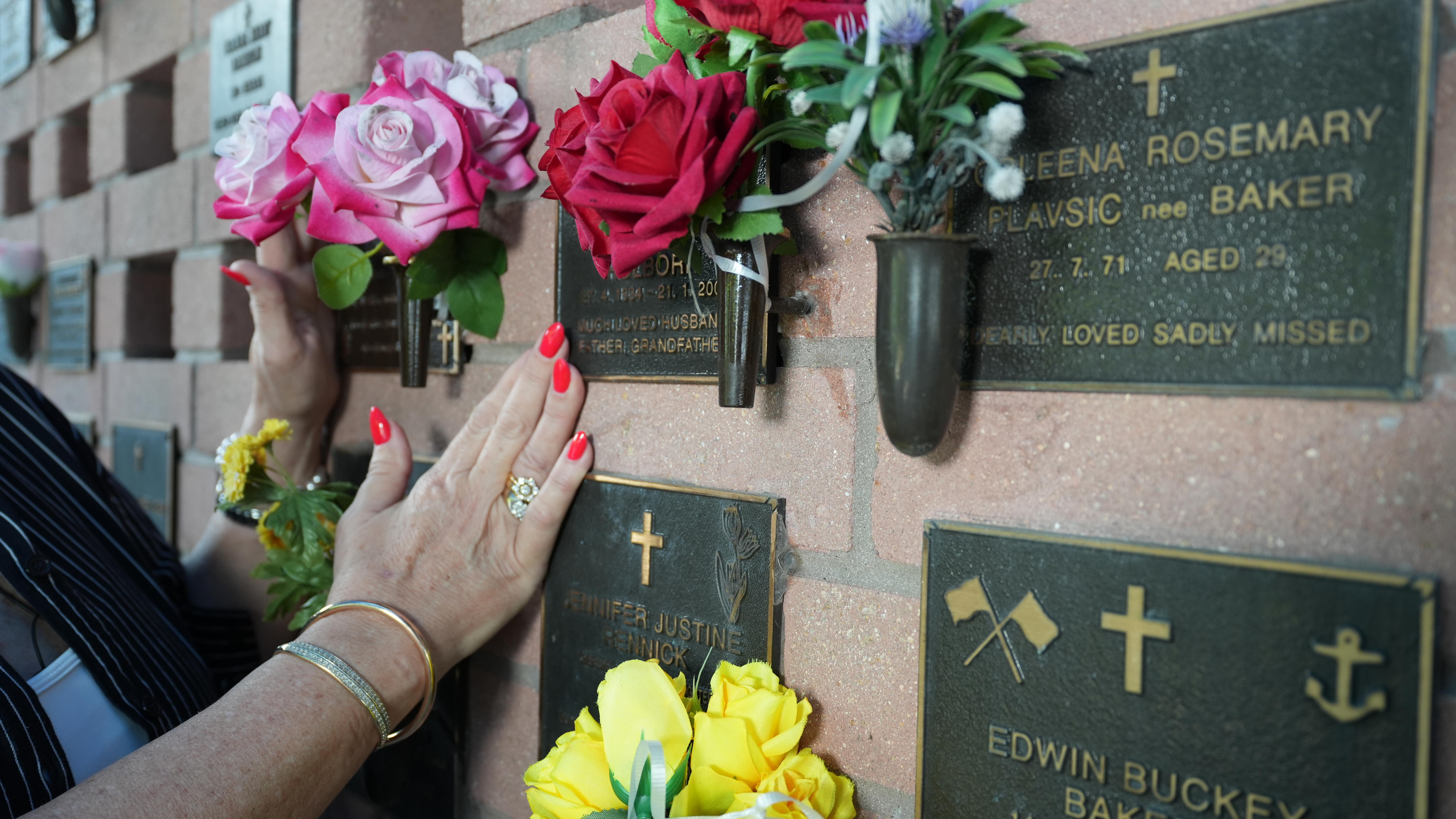 A woman rests her hands on plaques on a columbarium wall