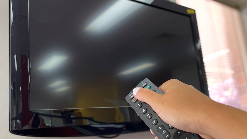 A hand holding a remote up to a black television screen.