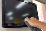 A hand holding a remote up to a black television screen.