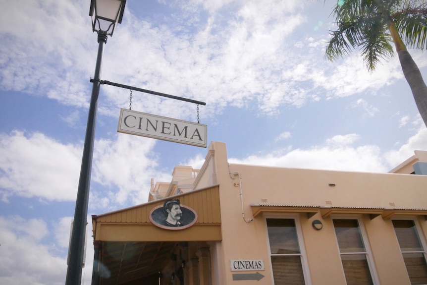 An old-fashioned cinema sign hanging from a lamp post.