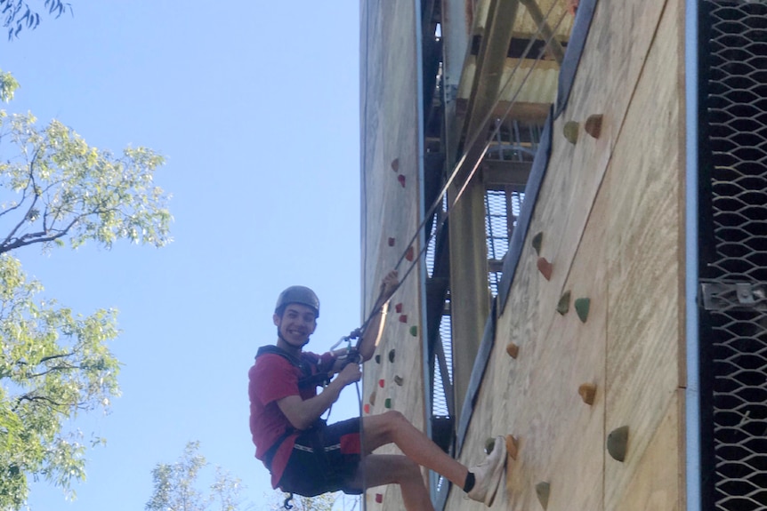 Teenage boy does mock rock climbing. He is smiling.