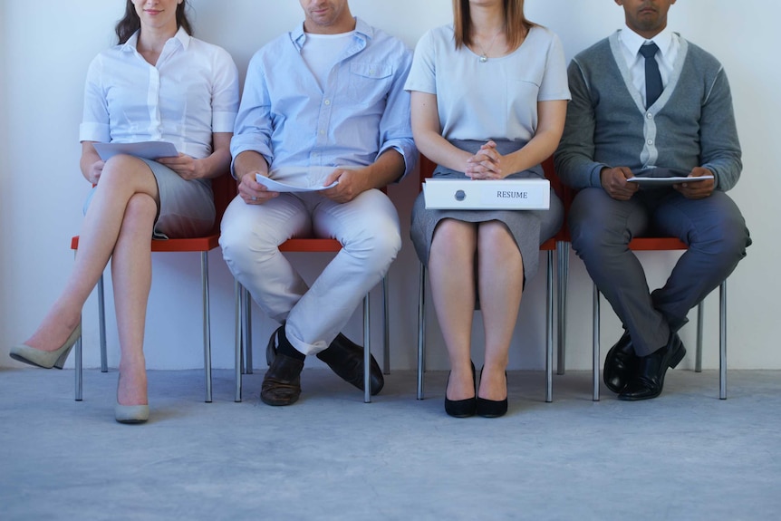 Four people sit on chairs, holding a resume. Their faces are not in frame.