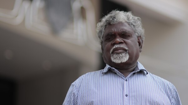 An Aboriginal man in a dress shirt looks down toward the camera.
