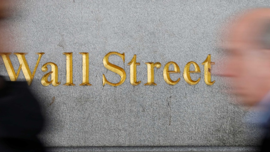 People walk past a Wall Street sign near the New York stock exchange.