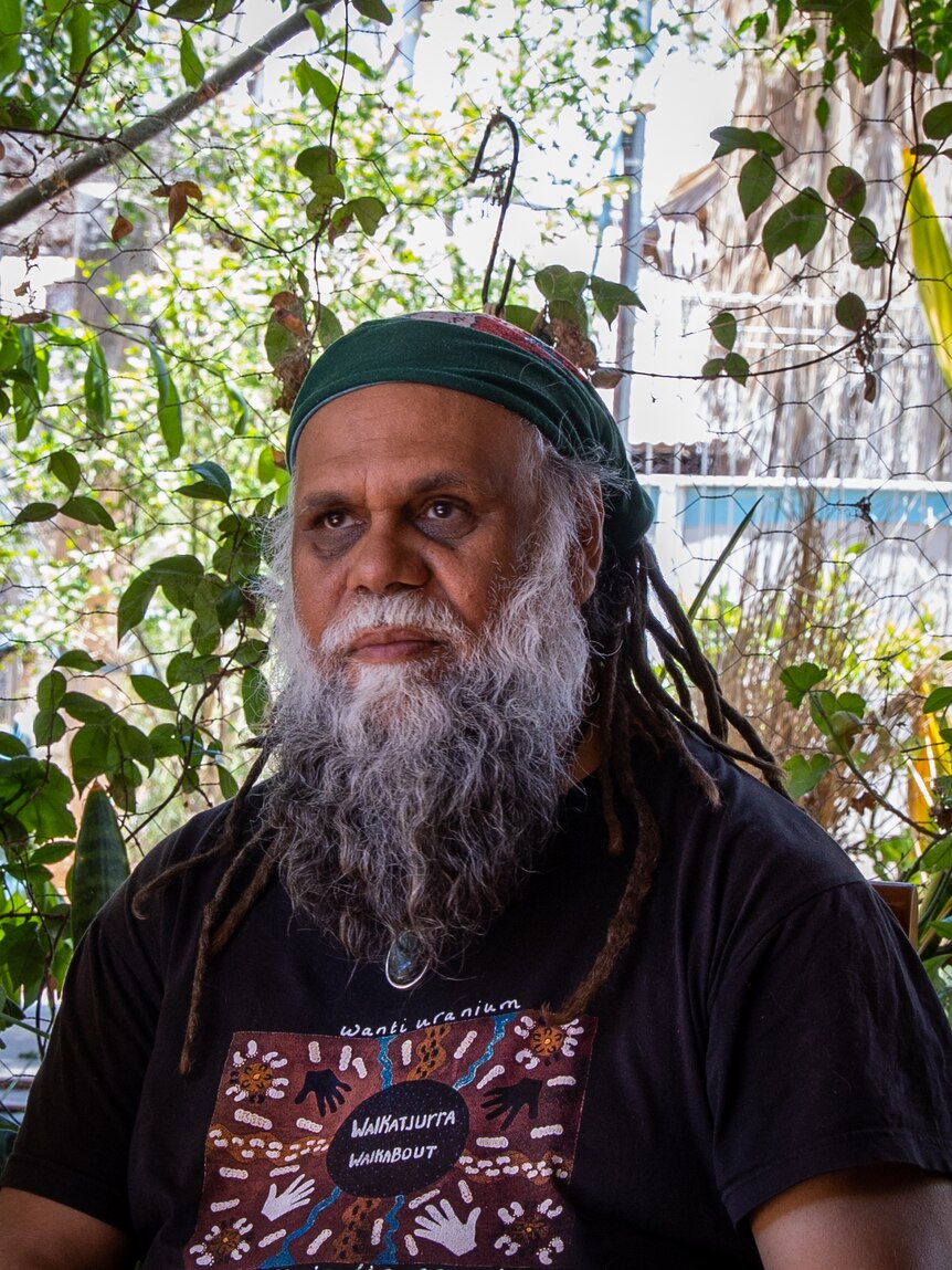Portrait of an older Indigenous Australian man with a grey beard, a headband and dreadlocks. 