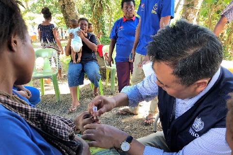 A woman holds a baby as it is given the polio vaccine in PNG