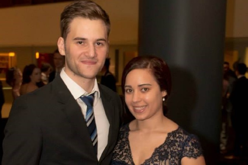 A man in black tie and a woman wearing a lacy black dress stand together smiling