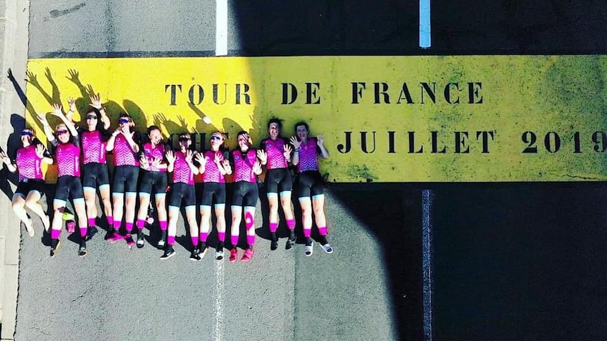 Ten woman lie on the road on a sign that says Tour De France Juillet 2019