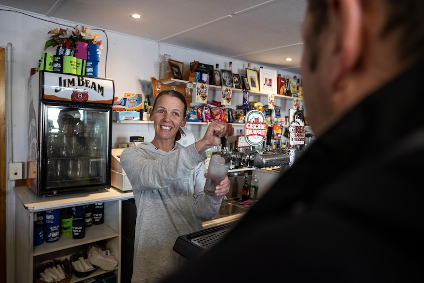 Jodie O’Byrne smiling and pouring a beer at the pub she works at. 