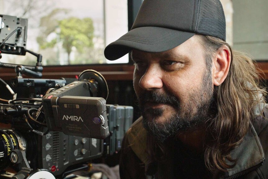 Filmmaker Warwick Thornton stands behind a video camera.