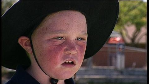 Child with flushed red cheeks wears sun hat
