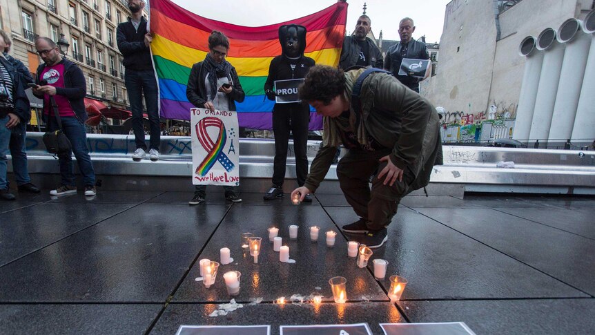 People holding rainbow flags and placing candles on the ground at a vigil in Paris.