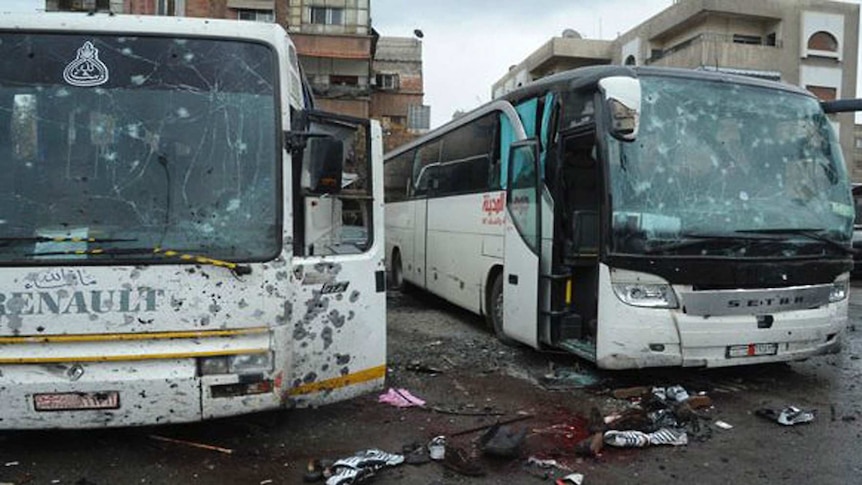 Two buses dotted with bullet holes, blood-soaked streets with shoes lying on the road nearby, buildings in the background