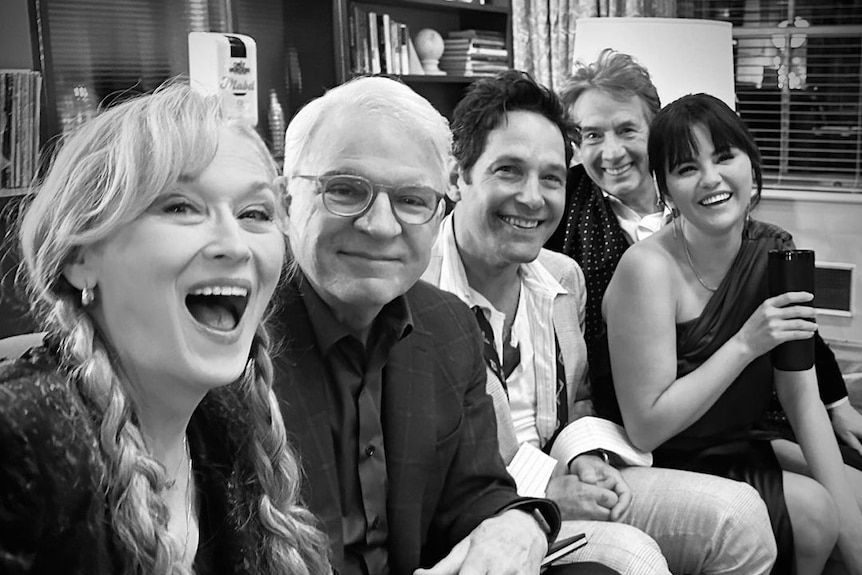 A black and white selfie of Meryl Streep, Steve Martin, Paul Rudd, Selena Gomez and Martin Short smiling on a couch.