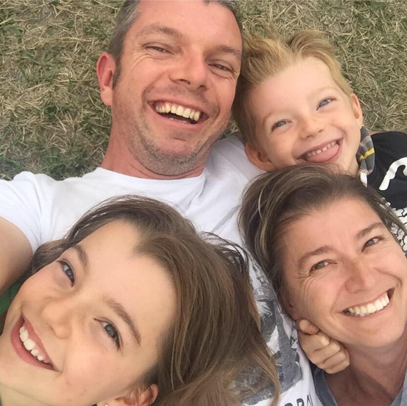 Israel Smith in a selfie with his wife and two children, lying on grass.