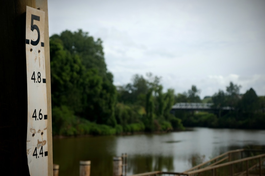 Numbers up the side of a pole with a river and bridge in the background