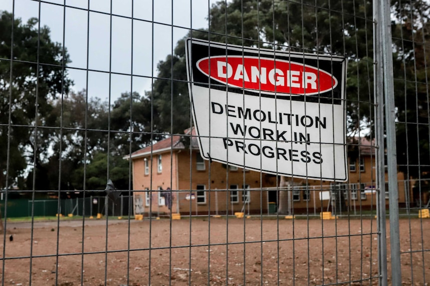 A demolition work in progress sign on a fence in front of a set of flats, which have graffiti on them.