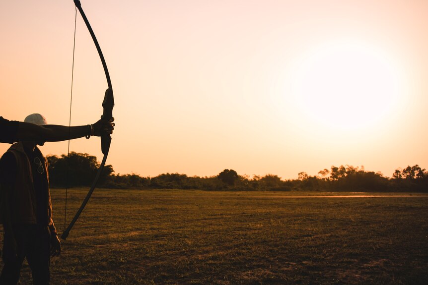 An archery bow in front of a sunset. The bow is not drawn. 