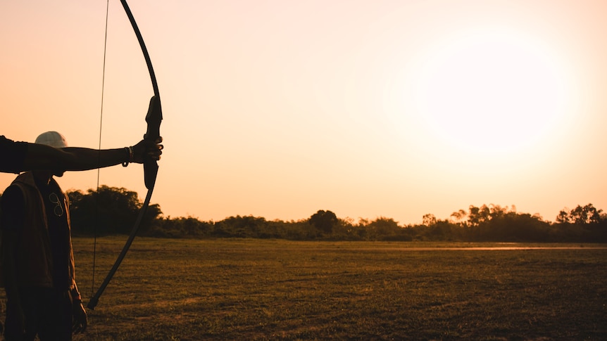 An archery bow in front of a sunset. The bow is not drawn. 