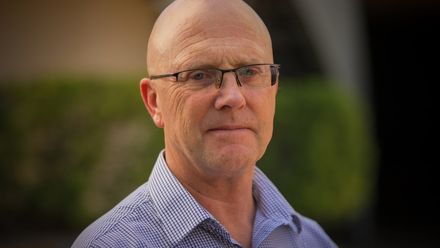 Bald man wearing a blue and white checked business shirt and glasses.