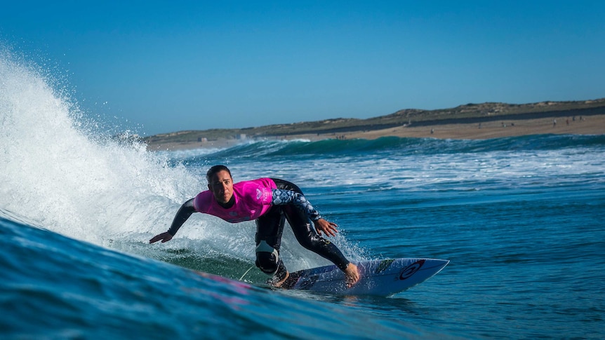 Action image of surfer making a turn on a wave with the shoreline in the background.