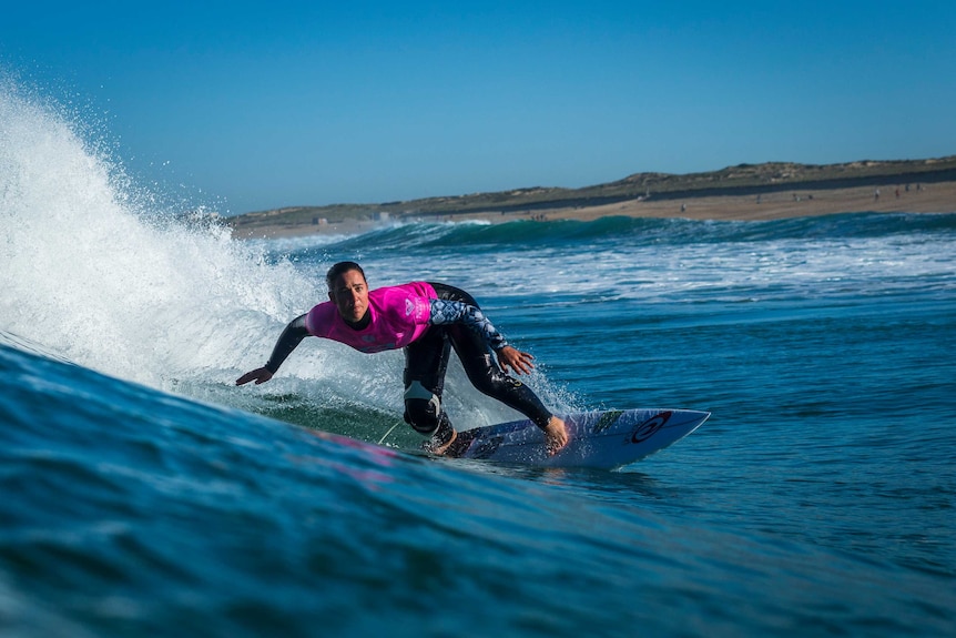 Action image of surfer making a turn on a wave with the shoreline in the background.