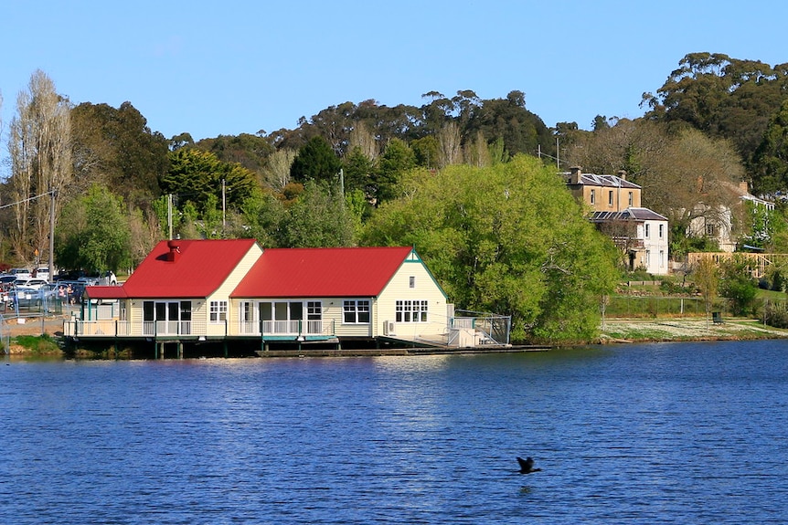 a boat house on a lake, surrounded by trees, seen from across the lake