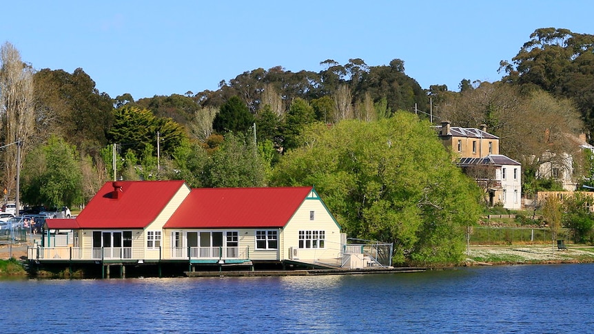 a boat house on a lake, surrounded by trees, seen from across the lake.
