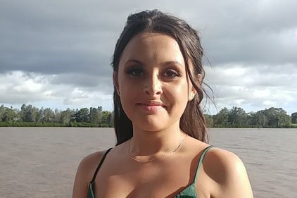 Young girl with dark hair poses in green formal dress, with river in the background 