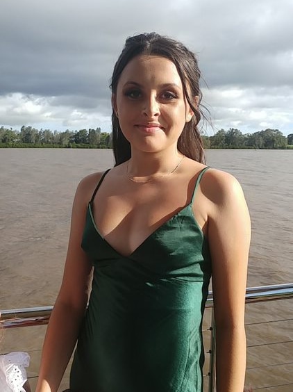 Young girl with dark hair poses in green formal dress, with river in the background 