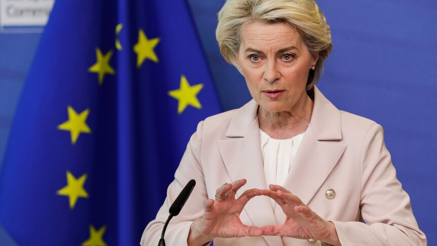 European Commission President Ursula von der Leyen gestures in from of EU flags.