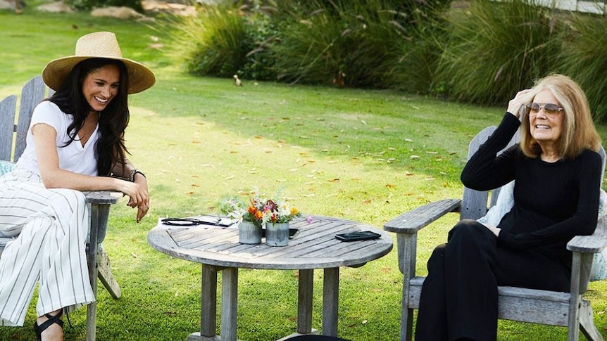 Dark-haired woman dressed in white sits in garden with older blonde-haired women dressed in black