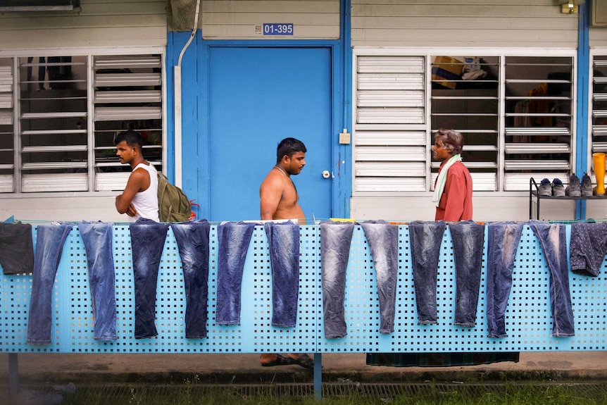 Men walk along a balcony where a row of jeans are being dried in the sun