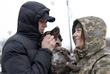 A man in a black hood and a woman in a camo print hood holding a dog. 