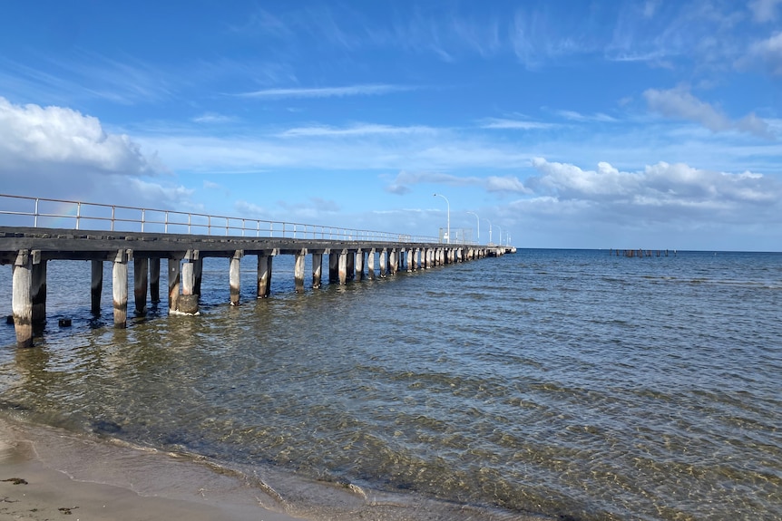 Altona Pier in Melbourne's south-west is pictured on a sunny day with blue skies and clouds in the background.