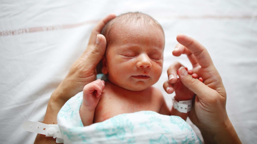 Close-up of a newborn baby in mother's hands, in hospital.