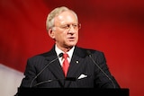Andrew Peacock speaks at a lectern in front of a red background.