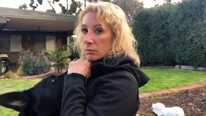 Melbourne dog trainer Trish Harris kneels in the backyard patting a black dog while looking into the camera