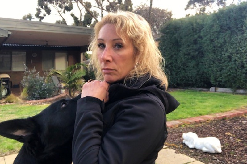 Melbourne dog trainer Trish Harris kneels in the backyard patting her black German Shepherd while looking into the camera
