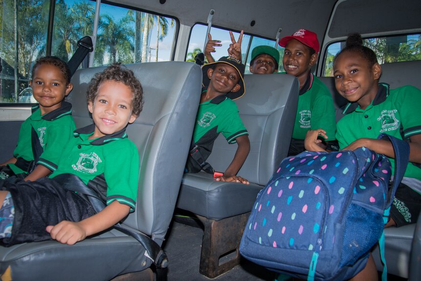 Primary school children smile while sitting in a minivan waiting to be taken to school.