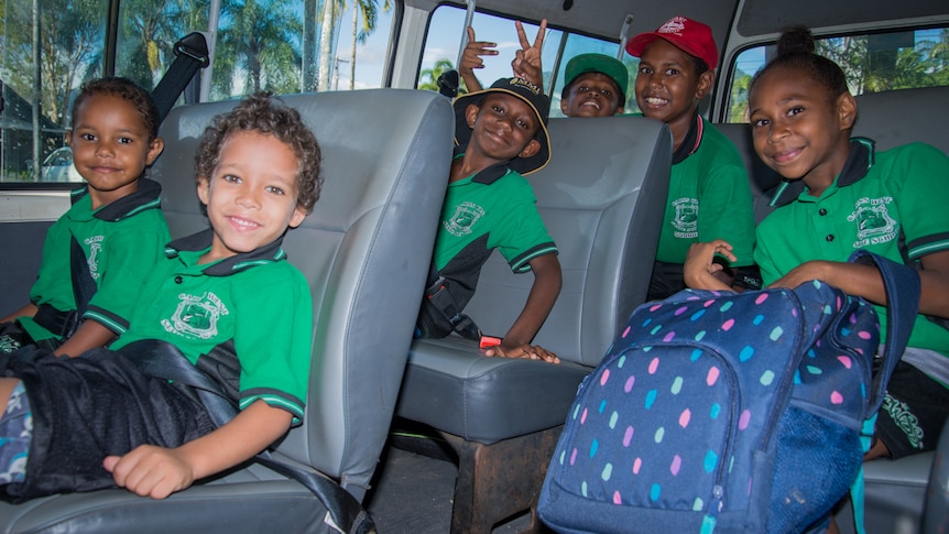 Primary school children smile while sitting in a minivan waiting to be taken to school.